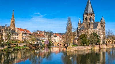 Fluss mit historischer Kirche und Gebäuden im Hintergrund, blauer Himmel.