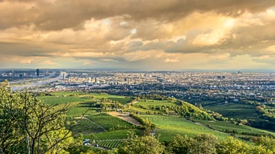 twerenbold_79621.jpg Panoramablick auf eine Stadt mit grünen Hügeln und dramatischem Himmel.