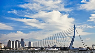 Moderne Schrägseilbrücke über Wasser mit Stadtgebäuden im Hintergrund.