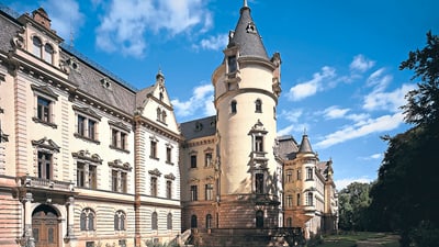 Historisches Schloss mit Türmen und dekorativer Fassade unter blauem Himmel.
