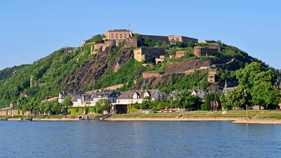 twerenbold_56341.jpg Festung auf grünem Hügel am Flussufer.