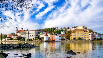 twerenbold_92870.jpg Blick auf bunte Gebäude am Flussufer mit bewölktem Himmel.
