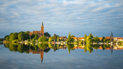 mecklenburgische-seenplatte.jpg Stadtlandschaft am See mit Kirche und Wolkenhimmel.
