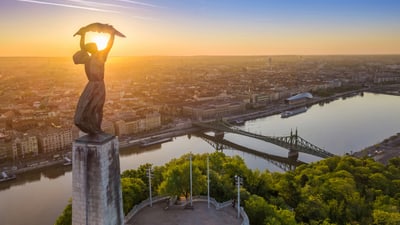 Freiheitsstatue auf Hügel mit Fluss und Stadt im Sonnenuntergang.
