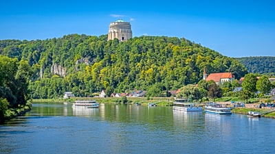 twerenbold_79386.jpg Ruhiger Fluss mit Schiffen, Hügel und Gebäude im Hintergrund.