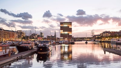 twerenbold_78098.jpg Hafenansicht mit Sonnenuntergang und modernem Gebäude.