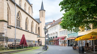 bonn.jpg Stadtstrasse mit alten Gebäuden, Sitzgelegenheiten im Freien und Sonnenschirmen.