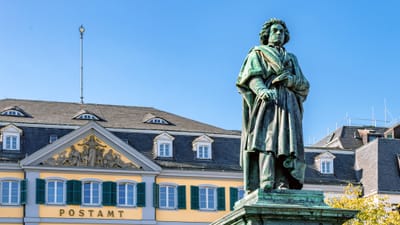 das-beethoven-denkmal-auf-dem-muensterplatz-erinnert-an-den.jpg Statue vor historischem Gebäude mit gelben und weissen Fassaden.
