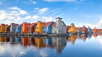groningen.jpg Bunte Häuser spiegeln sich in ruhigem Wasser unter blauem Himmel.