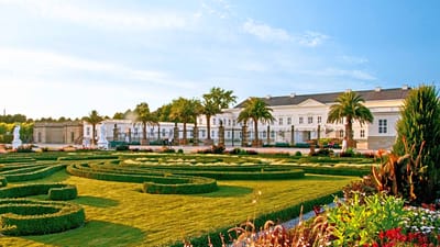 twerenbold_38060.jpg Barockgarten vor einem grossen, weissen Gebäude bei Sonnenschein.