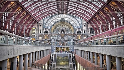 Innenansicht des Bahnhofs mit gewölbtem Glasdach und Zügen.