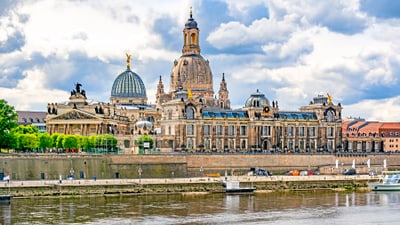 twerenbold_77465.jpg Historisches Gebäude an einem Flussufer mit bewölktem Himmel.