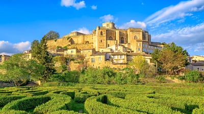 dorf-grignan.jpg Historische Burg auf einem Hügel mit Labyrinth aus Hecken im Vordergrund.