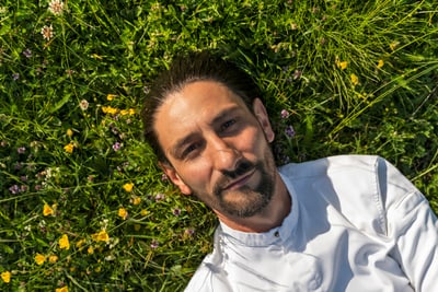 das-excellence-gourmetfestival-10.jpg Mann in weissem Hemd liegt auf Wiese mit Blumen.