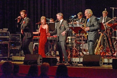 Band auf der Bühne mit Sängern und Musikern in formeller Kleidung.