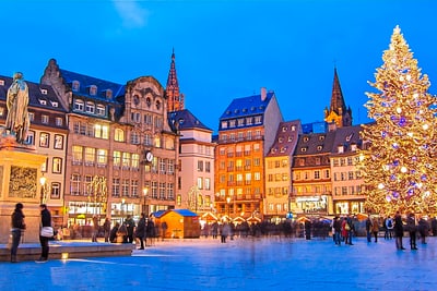 Weihnachtsbaum und Statuen auf beleuchtetem Platz bei Dämmerung.