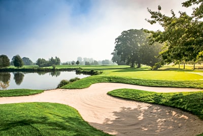 golf-resort-bad-griesbach.jpg Golfplatz mit Sandbunker und Teich bei Sonnenschein.
