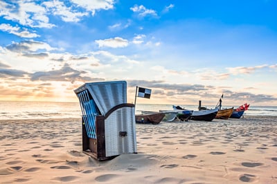 strandkorb-an-der-ostseekueste.jpg Sonnenuntergang am Strand mit Strandkorb und Fischerbooten.