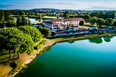 Luftaufnahme eines Gebäudes am See mit Bäumen und Landschaft.