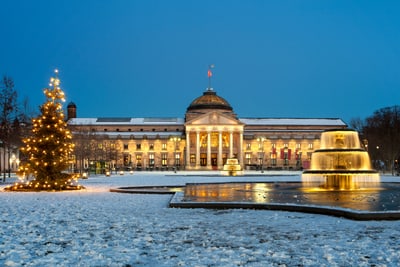 Beleuchtetes historisches Gebäude und Brunnen bei Schnee und Weihnachtsbaum.