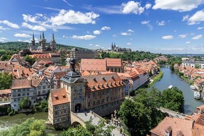 Stadtansicht mit Fluss und historischen Gebäuden vor blauem Himmel.