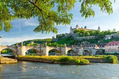 Alte Steinbrücke über Fluss mit Festung im Hintergrund.