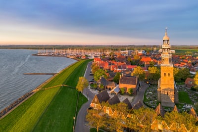 hindeloopen-am-ijsselmeer.jpg Luftaufnahme einer Küstenstadt mit einem Kirchturm und Yachthafen bei Sonnenuntergang.