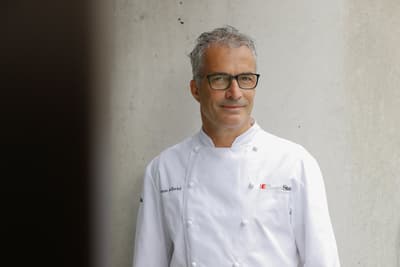 das-excellence-gourmetfestival-10.jpg Mann in weissem Kochmantel steht vor einer Betonwand.