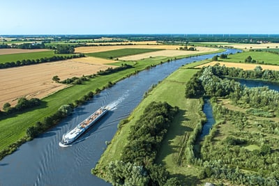 Luftaufnahme eines Flusses mit einem Schiff und umliegenden Feldern.