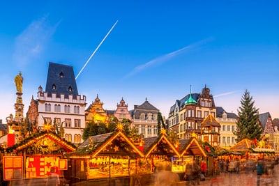 Weihnachtsmarktständen vor historischen Gebäuden bei Abenddämmerung.