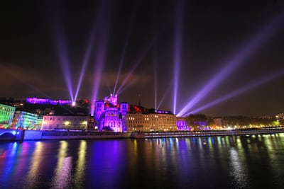 Nachts beleuchtete Gebäude mit Lichtsäulen am Fluss.