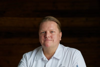 das-excellence-gourmetfestival-10.jpg Person in weissem Kochmantel sitzt an einem Holztisch.