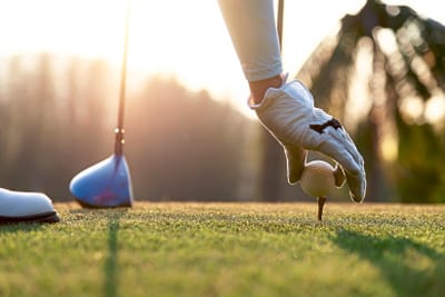 Nahaufnahme einer Hand mit Handschuh, die einen Golfball auf ein Tee setzt.