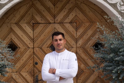 das-excellence-gourmetfestival-10.jpg Mann in weissem Hemd steht vor dekorativer Holztür.