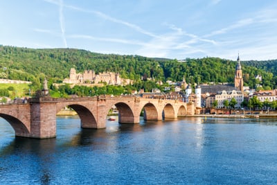 Steinbrücke über einen Fluss mit Stadt und Hügel im Hintergrund.
