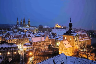 bamberg.jpg Verschneite Stadtansicht mit beleuchteten historischen Gebäuden bei Dämmerung.