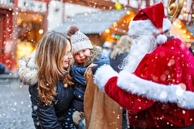 Kind und Frau treffen Weihnachtsmann auf verschneitem Weihnachtsmarkt.