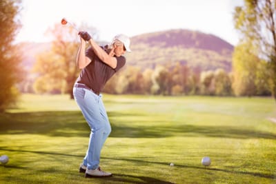 Person beim Golfschwung auf einem Golfplatz vor Bergkulisse.