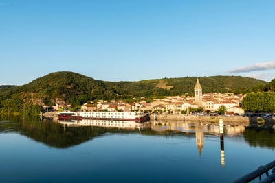 Flusspanorama mit Dorf und Hügeln im Hintergrund.