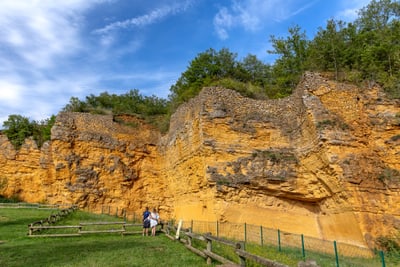 Besucher betrachten gelbe Steinmauer mit Bäumen oben.