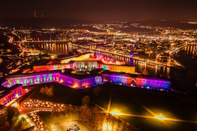 twerenbold_106258.jpg Drohnenansicht einer beleuchteten Festung und Stadt bei Nacht.