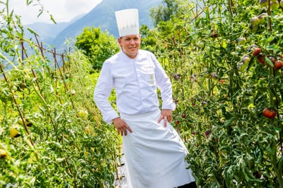 das-excellence-gourmetfestival-10.jpg Koch im weissen Outfit steht zwischen Tomatenpflanzen im Freien.