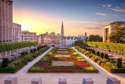 Gartenanlage mit geometrischen Beeten und Stadtblick im Hintergrund bei Sonnenuntergang.