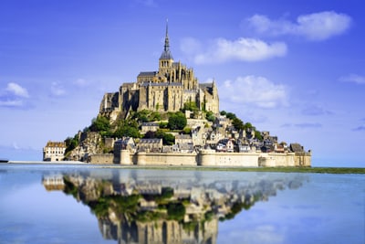 Mont Saint-Michel auf felsiger Insel im Meer, blauem Himmel.