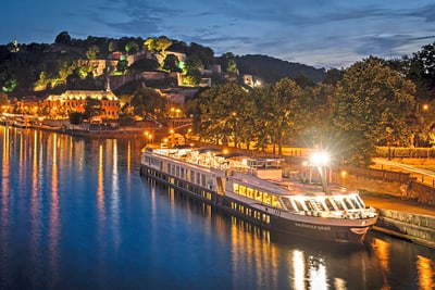 excellence-pearl.jpg Beleuchtetes Flussschiff bei Nacht, umgeben von Hügeln und Bäumen.