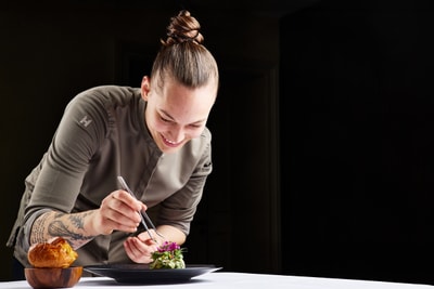 das-excellence-gourmetfestival-10.jpg Person in Kochjacke verziert ein Gericht auf einem Tisch.