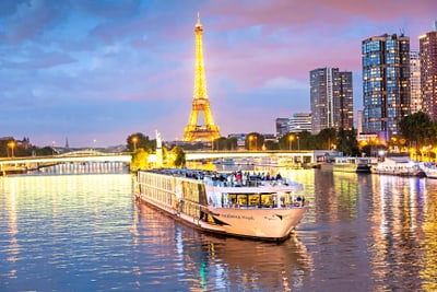 Beleuchtetes Schiff auf der Seine vor Eiffelturm bei Abenddämmerung.
