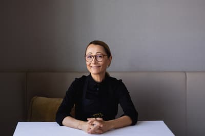Frau mit Brille und dunklem Oberteil sitzt an einem Tisch.