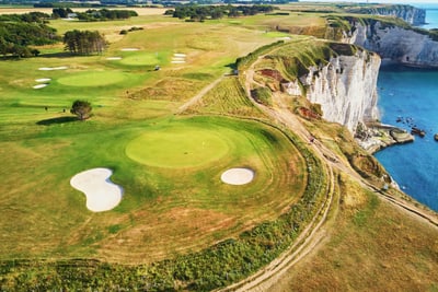Landschaft mit Küstenklippen, grünen Feldern und Golfplätzen neben dem Meer.