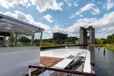 Boot im Kanal vor Schiffshebewerk unter blauem Himmel.